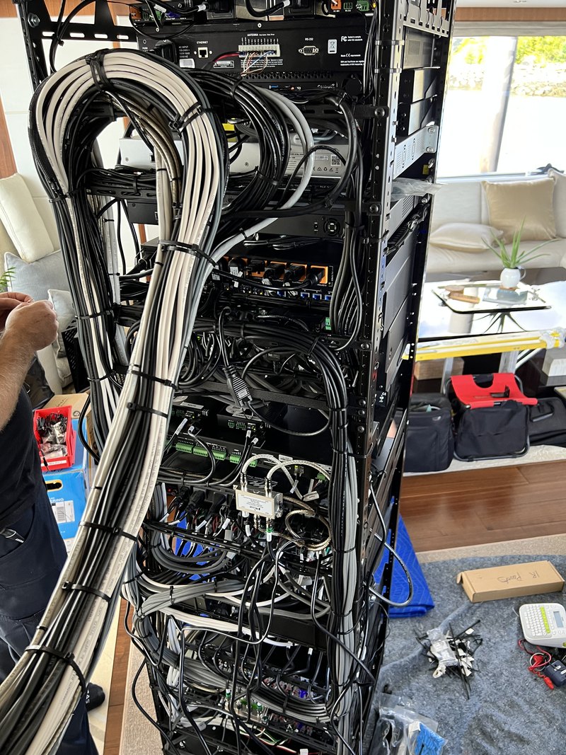 Rear view of the rack mid-termination showing meticulously bundled and tie-wrapped white and black cable looms feeding matrix switchers, control processors, and power gear.