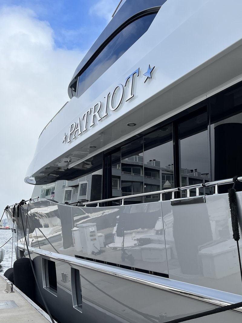 Low dramatic angle up the glossy bow with the raised stainless 'PATRIOT' name lettering and mirror-polished dark superstructure glass.
