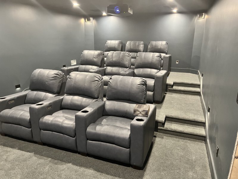 Finished theater with three rows of gray power recliners, acoustic wall panels, and the projector glowing; content is excellent but the file is stored rotated.